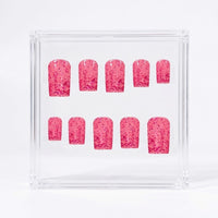A set of ten pink glitter press-on nails displayed on a clear acrylic stand against a white background.
