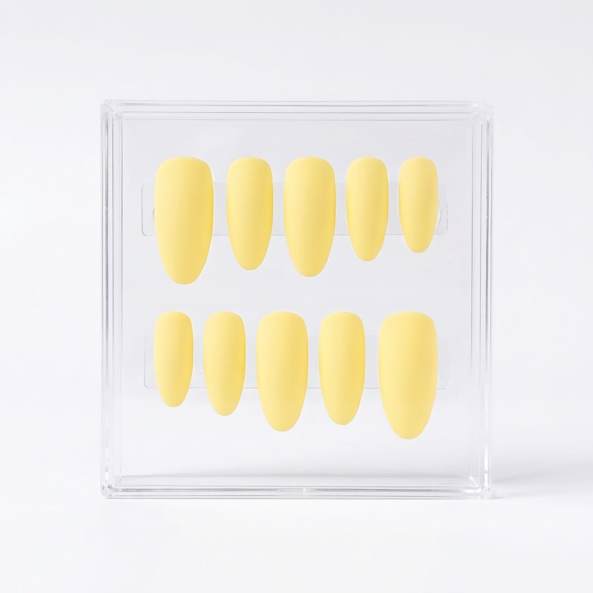 A set of ten pale yellow press-on nails arranged in two rows inside a clear acrylic display box on a white background.