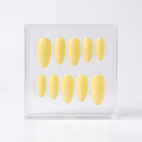 A set of ten glossy pale yellow press-on nails displayed inside a clear acrylic case on a white background.