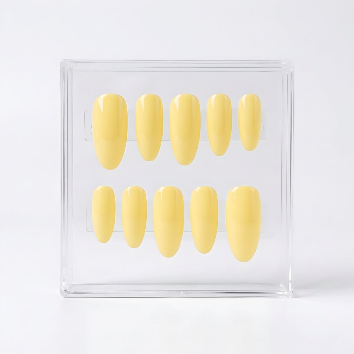 A set of ten glossy pale yellow press-on nails displayed inside a clear acrylic case on a white background.