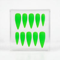 A set of ten bright neon green stiletto-shaped press-on nails arranged inside a clear acrylic display box on a white background.