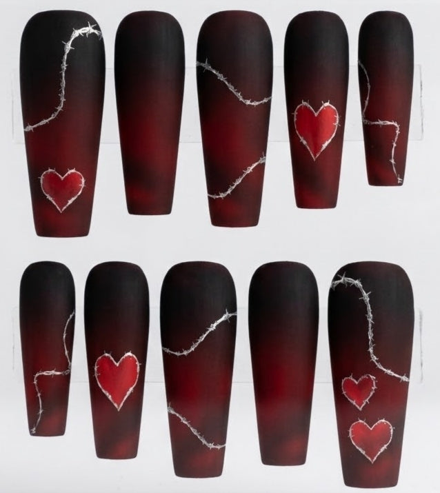 Ten coffin-shaped matte  press-on nails arranged in two rows on a white background. The nails have a dark red to black ombre gradient with silver barbed wire line art and red heart designs in varying sizes.