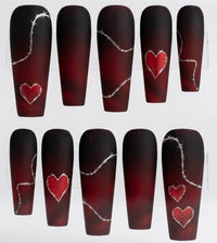Ten coffin-shaped matte  press-on nails arranged in two rows on a white background. The nails have a dark red to black ombre gradient with silver barbed wire line art and red heart designs in varying sizes.