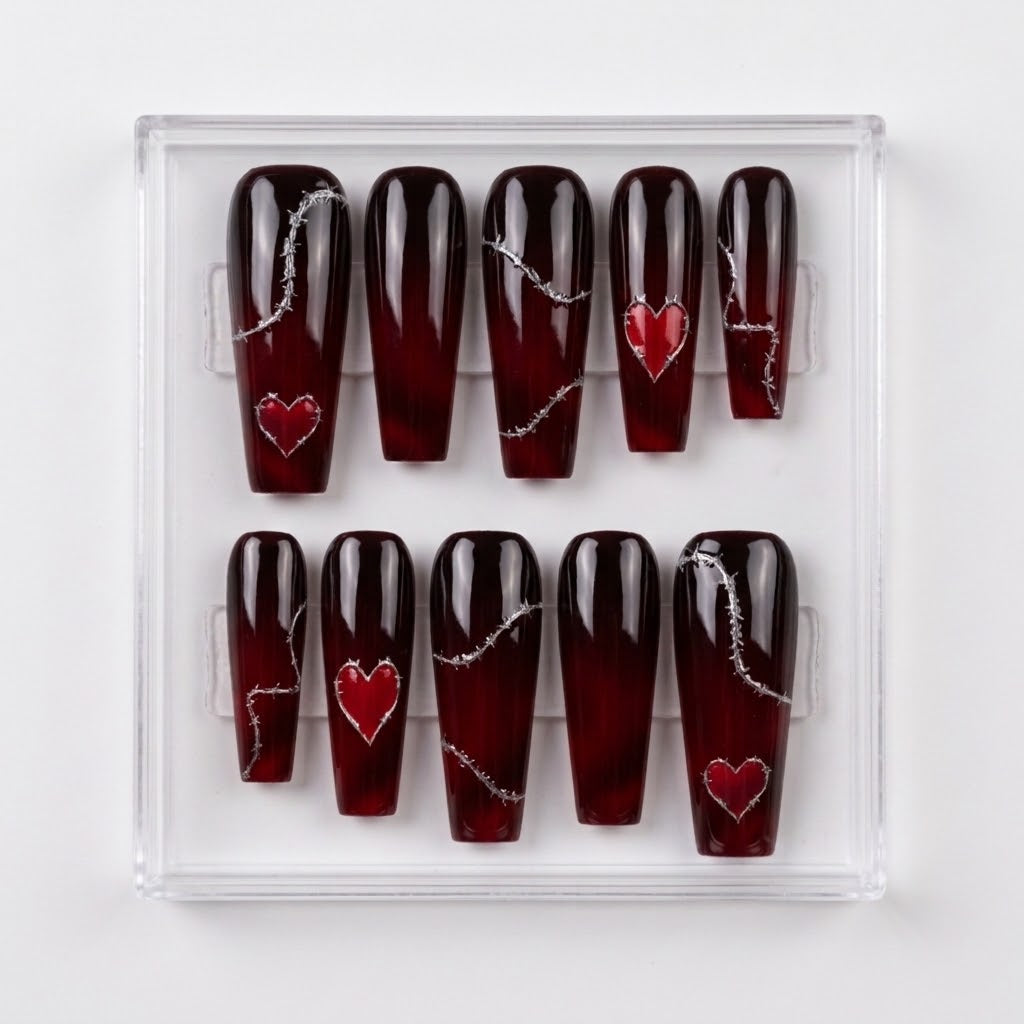 A set of coffin-shaped glossy press-on nails in a clear plastic display box. The nails have a glossy deep red-to-black ombre gradient with silver barbed wire details and red heart designs.
