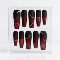 A set of ten coffin-shaped matte press-on nails displayed in a clear acrylic box. The nails feature a dark red and black ombre gradient with silver barbed wire line details and red heart designs.