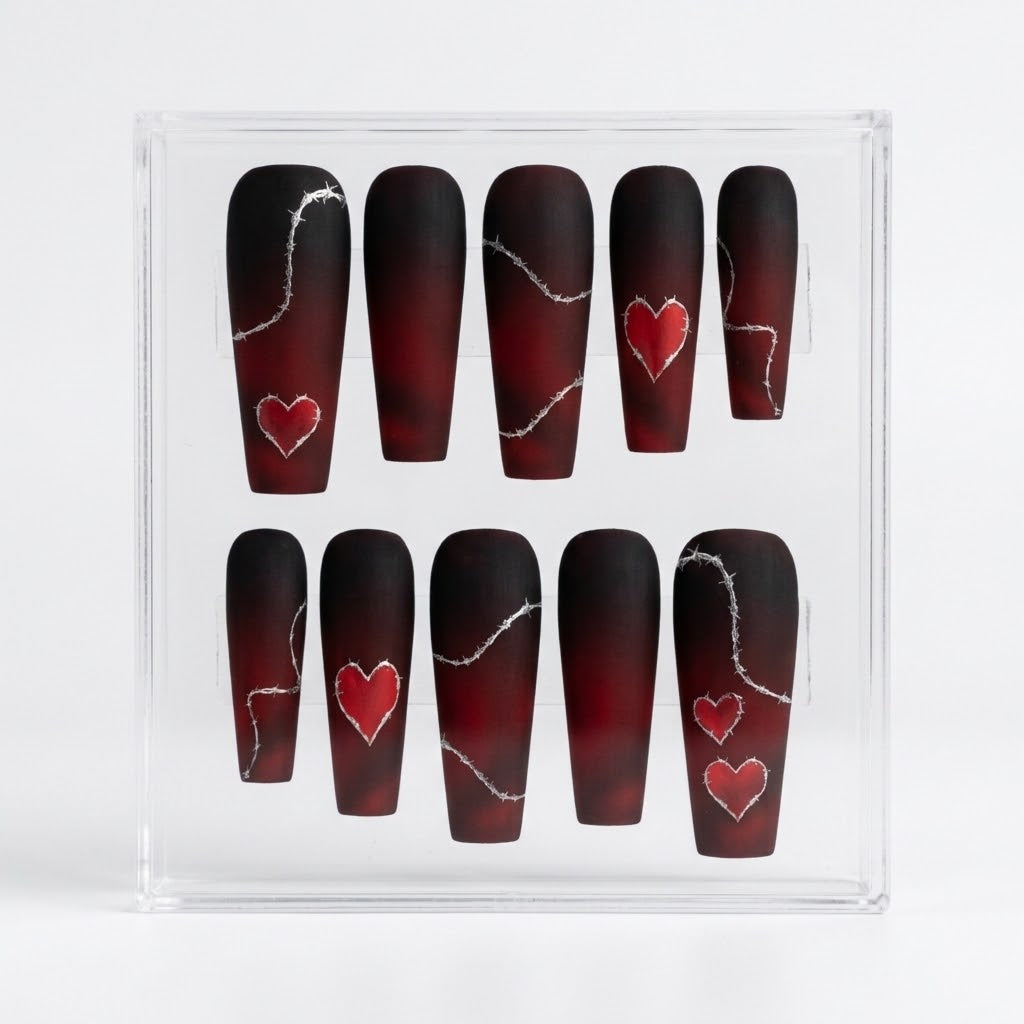A set of ten coffin-shaped matte press-on nails displayed in a clear acrylic box. The nails feature a dark red and black ombre gradient with silver barbed wire line details and red heart designs.
