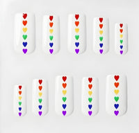 Set of 10 square glossy white press on nails with small rainbow hearts running down the centre. Displayed in a  clear display case on a white background.
