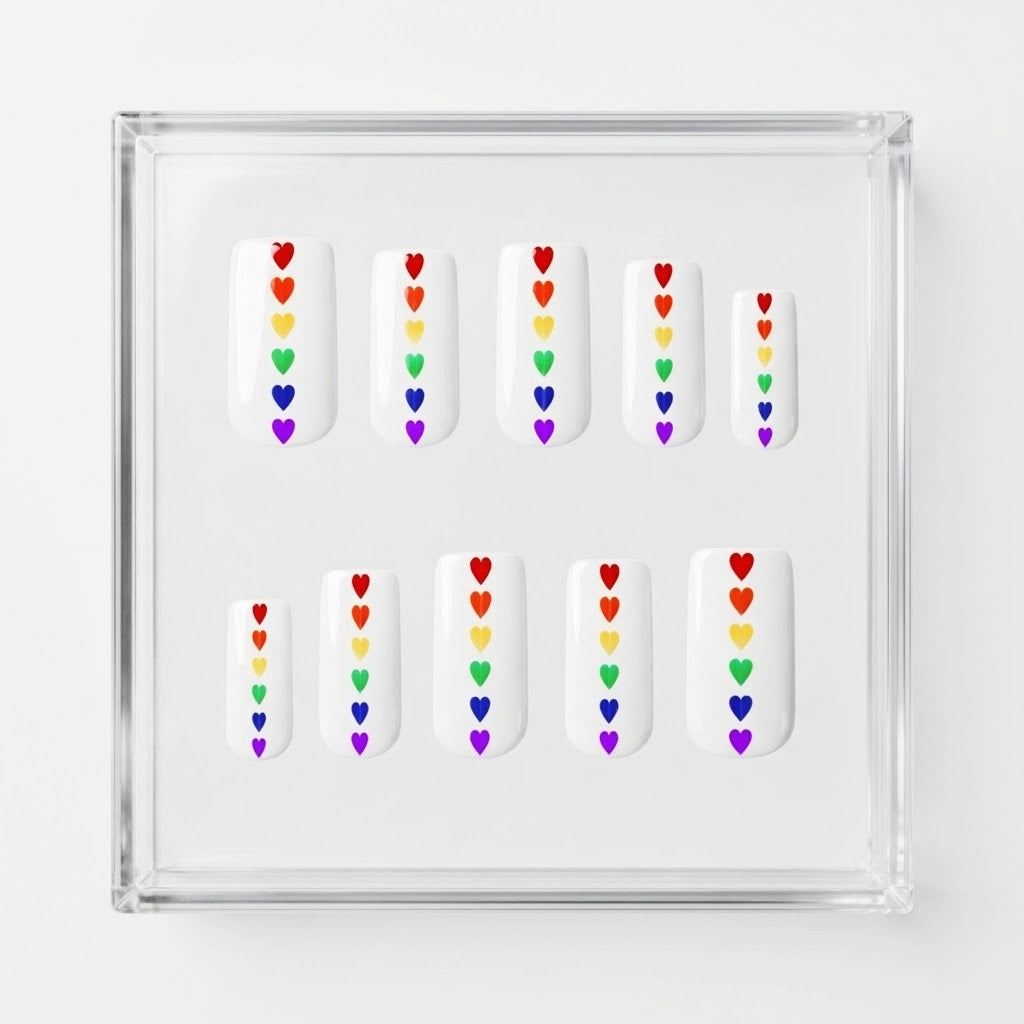 Set of 10 square glossy white press on nails with small rainbow hearts running down the centre. Displayed in a  clear display case on a white background.