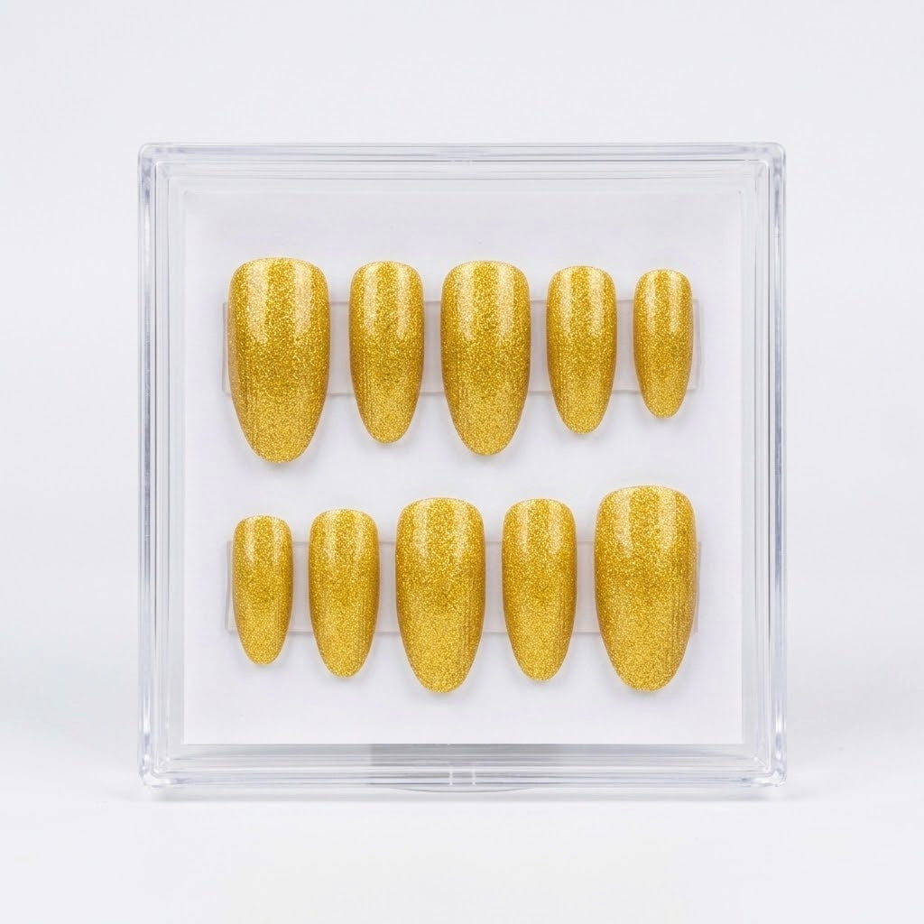 A set of glittery gold press-on nails displayed in a clear square plastic case against a white background.