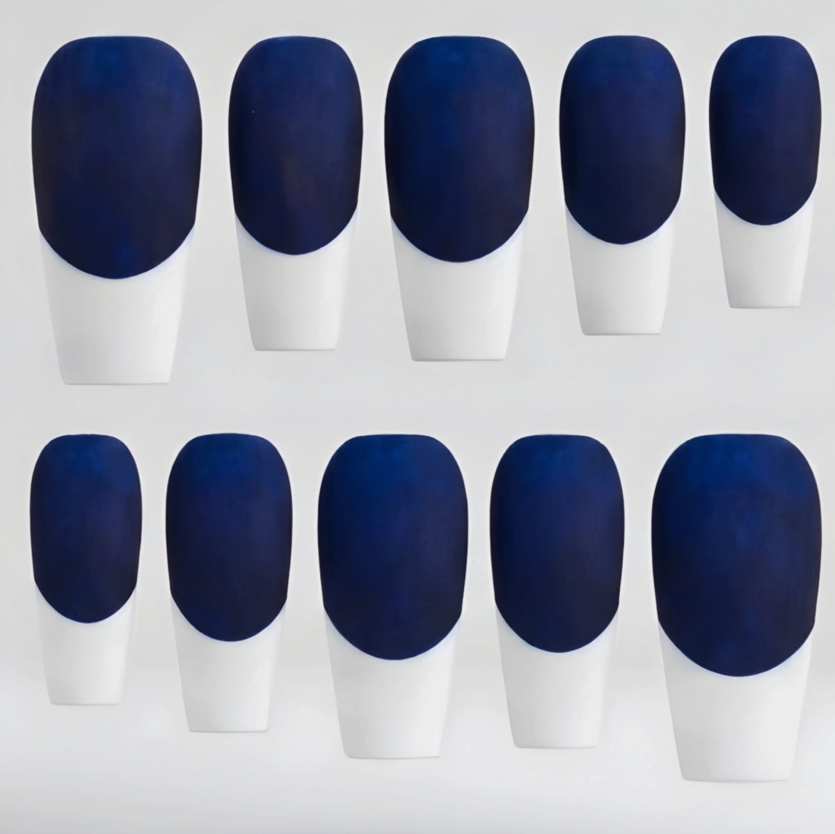 Ten false press-on nails arranged in two rows of five, featuring a dark navy blue base and white French-tips, on a light gray background.