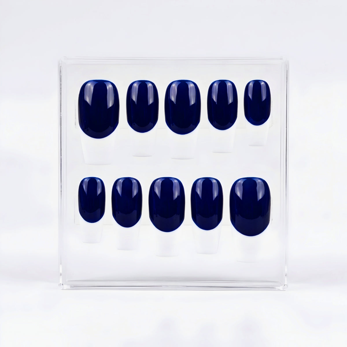 A set of ten press-on nails in a glossy deep navy blue base and white french tips, displayed inside a clear plastic rectangular box on a white background.
