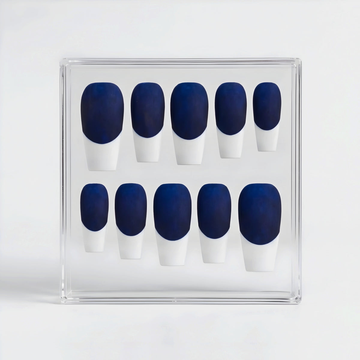 A set of ten press-on nails arranged in a clear plastic display box, featuring a deep navy blue base and white French tips.