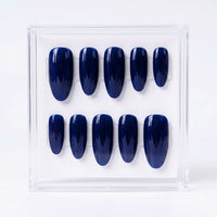 A set of ten glossy dark blue press-on nails displayed in a clear acrylic case against a white background.