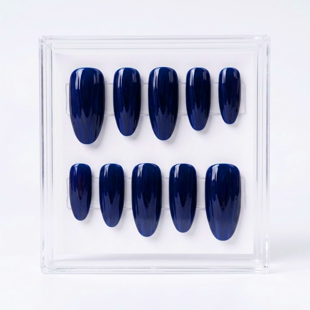 A set of ten glossy dark blue press-on nails displayed in a clear acrylic case against a white background.