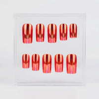 A set of ten press-on nails displayed in a clear acrylic case against a white background. The nails have a chrome metallic, iridescent orange finish with pink hues.