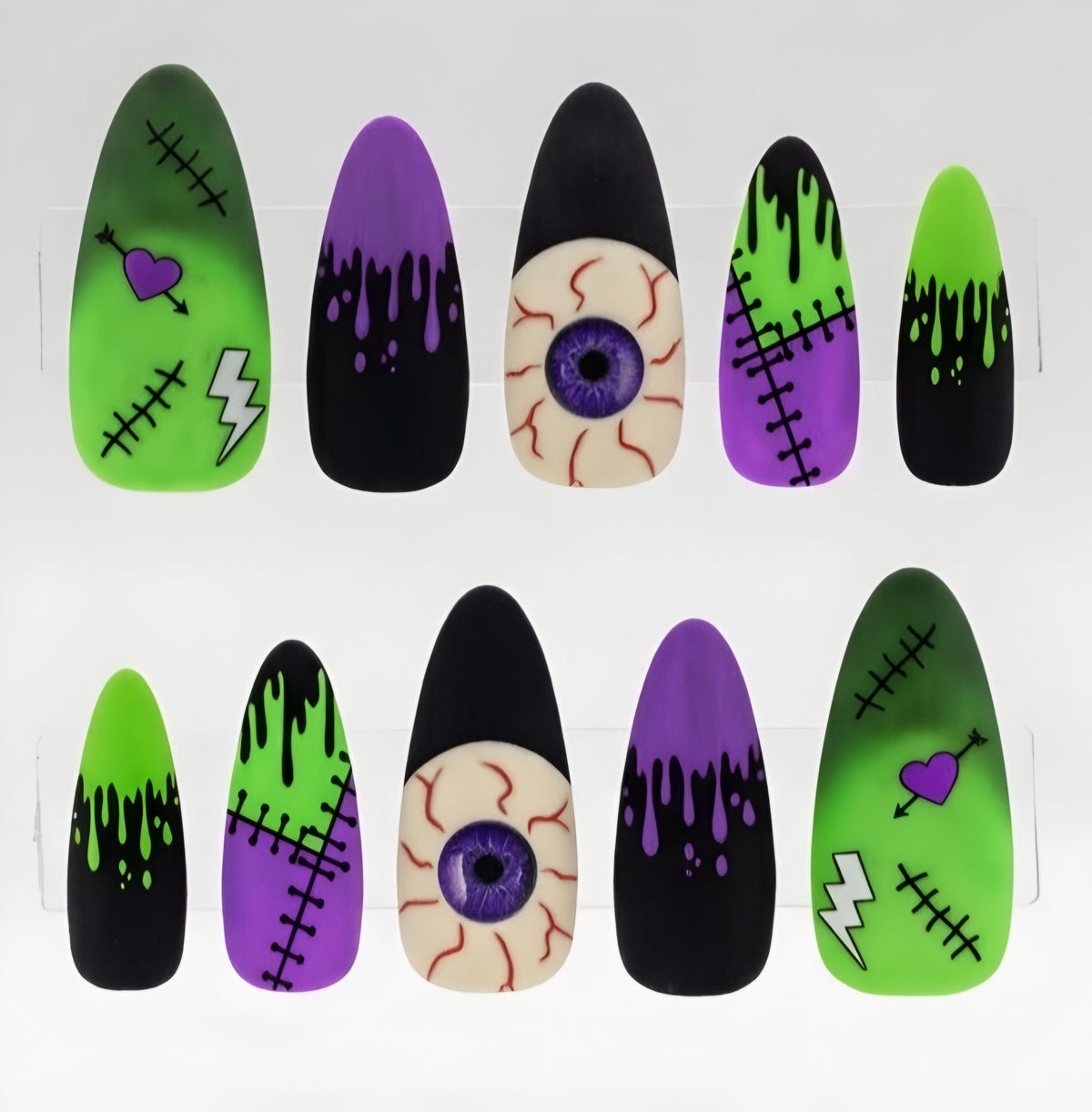A set of Halloween-themed false press-on nails arranged in two rows on a white background. The designs include green and black Frankenstein-style nails with stitches and lightning bolts, purple and black dripping witch nails, a beige and purple eyeball nail, and a green and black zombie-style nail with a purple heart.