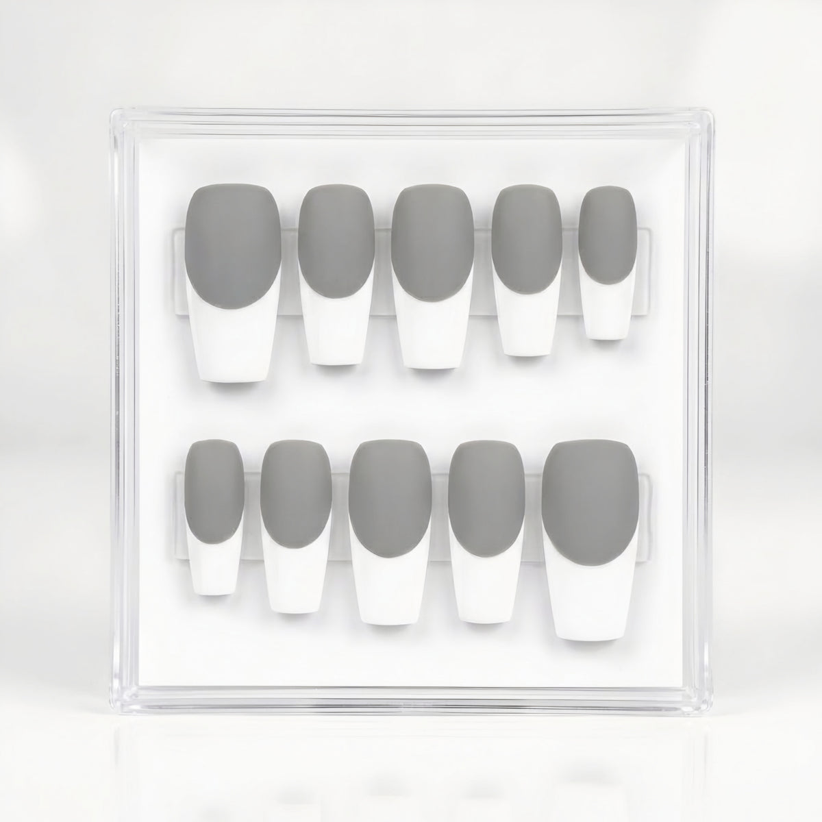A set of 10 press-on nails in a clear acrylic display case, featuring a classic French manicure with medium gray upper halves and white lower halves.