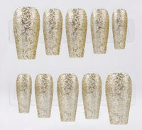 Ten coffin-shaped press-on nails with a textured glitter finish in champagne gold displayed on a clear plastic stand against a white background.