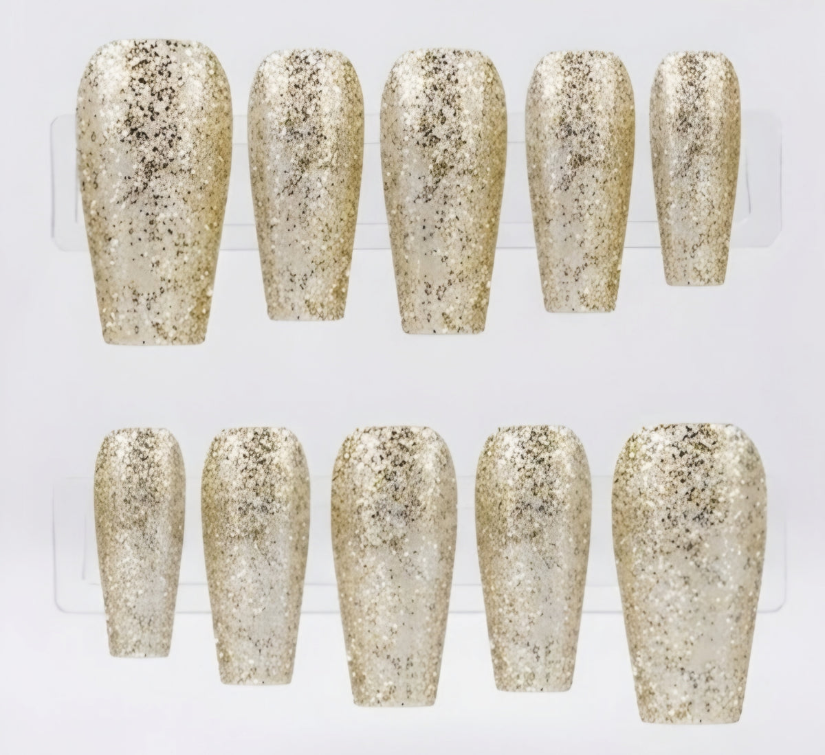 Ten coffin-shaped press-on nails with a textured glitter finish in champagne gold displayed on a clear plastic stand against a white background.