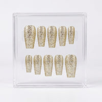 A set of glittery gold press-on nails displayed inside a clear acrylic case on a white background.