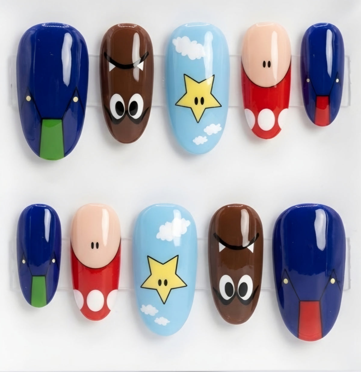 Ten glossy press-on nails arranged in two rows on a white background, featuring Nintendo-inspired Super Mario character designs including blue Goombas, a brown Goomba face, a light blue star on clouds, and a peach/red Mario face and body.