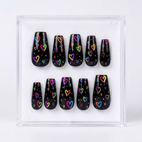 A set of ten glossy black press-on nails with colorful neon heart patterns, displayed inside a clear acrylic case on a white background.