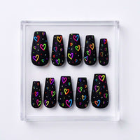 A set of ten ma black press-on nails with colorful neon heart patterns, displayed in a clear acrylic tray on a white background.te