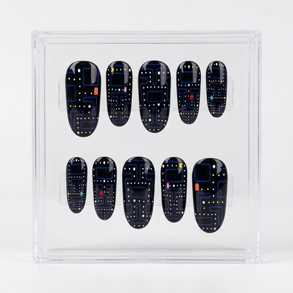 A set of ten glossy Pac-man themed press-on nails displayed inside a clear acrylic case on a white background. The nails are glossy black with a blue maze pattern, white dots, and small red and pink accents, mimicking a retro video game theme.