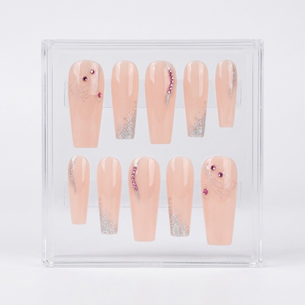 A set of 10 coffin shaped press on nails with a glossy peach nude base, silver glitter swirl details and silver glitter tips. The nails also have pink rinestones of them. The set is displayed in a clear case on a white background.