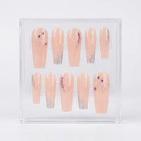 A set of 10 coffin shaped press on nails with a glossy peach nude base, silver glitter swirl details and silver glitter tips. The nails also have pink rinestones of them. The set is displayed in a clear case on a white background.