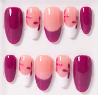 A set of ten glossy oval press-on nails displayed on clear plastic hangers against a white background. The design features a mix of glossy deep burgundy, white, and peachy nude with small red floral accents.