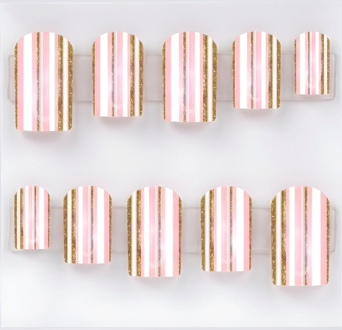Ten square press-on nails arranged in two rows on a clear plastic display card against a white background. The nails feature vertical stripes in light pink, white, and metallic gold glitter.