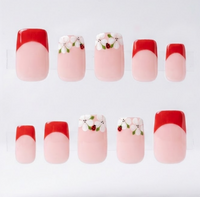 A set of ten false press-on nails arranged in two rows on a clear display stand against a white background. The nails feature a French tip design with a glossy red top half and a pale pink bottom half, with two designs decorated with small white flowers, ladybirds and green leaves.