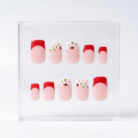 A set of 10 press-on nails displayed in a clear acrylic case against a white background. The nails feature a French tip design with a red half and a light pink full nail, with two additional designs featuring white flowers with ladybirds and green leaves.