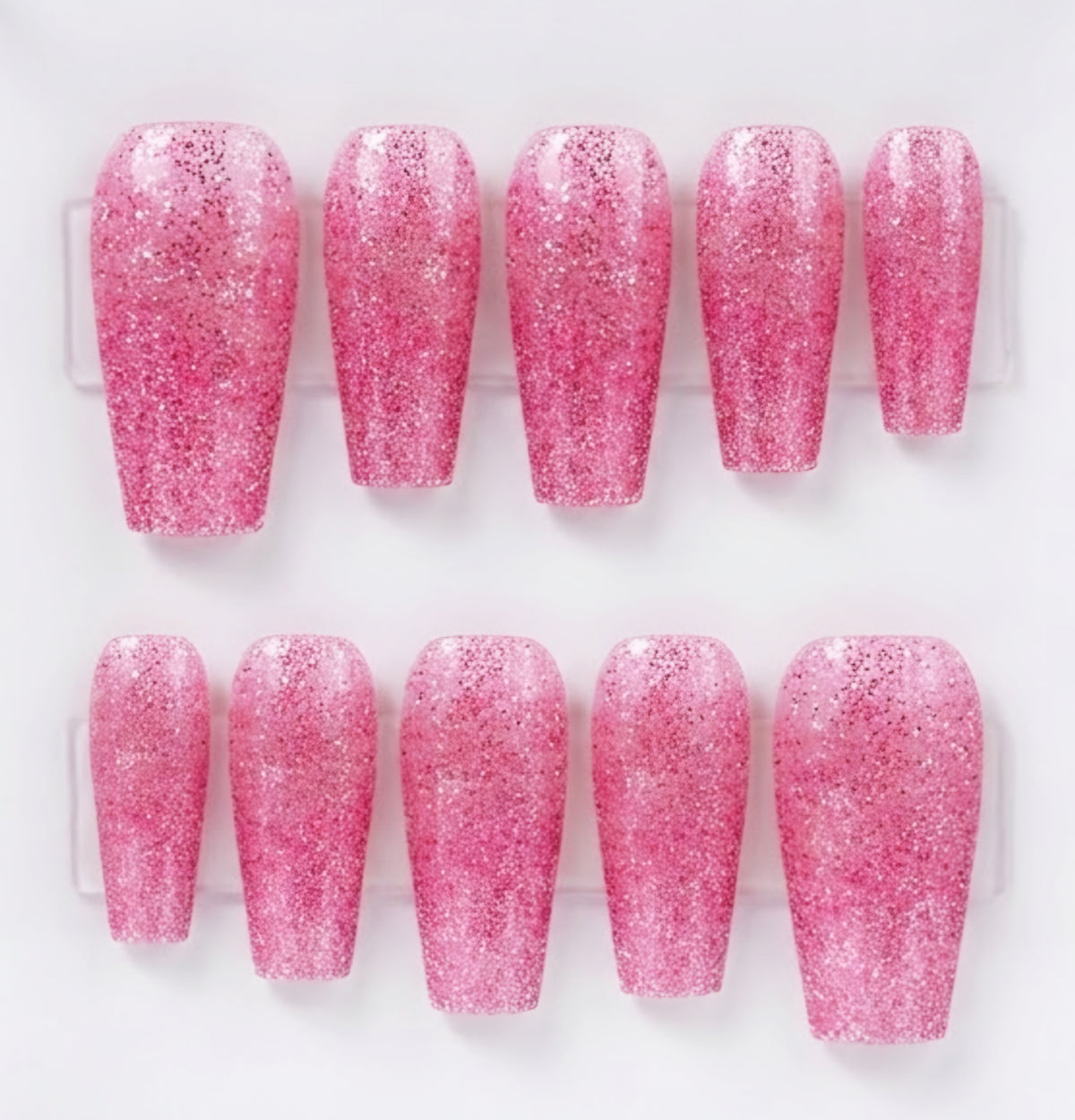 A set of ten pink glitter press-on nails arranged in two rows of five on a clear plastic display card against a white background.