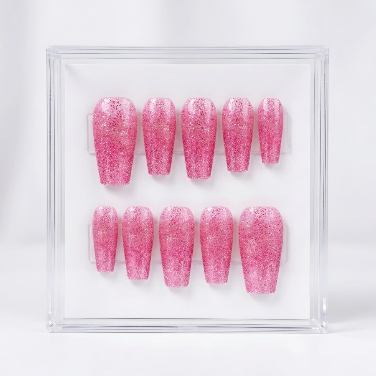 A set of ten glittery pink press-on nails displayed inside a clear acrylic case against a white background.