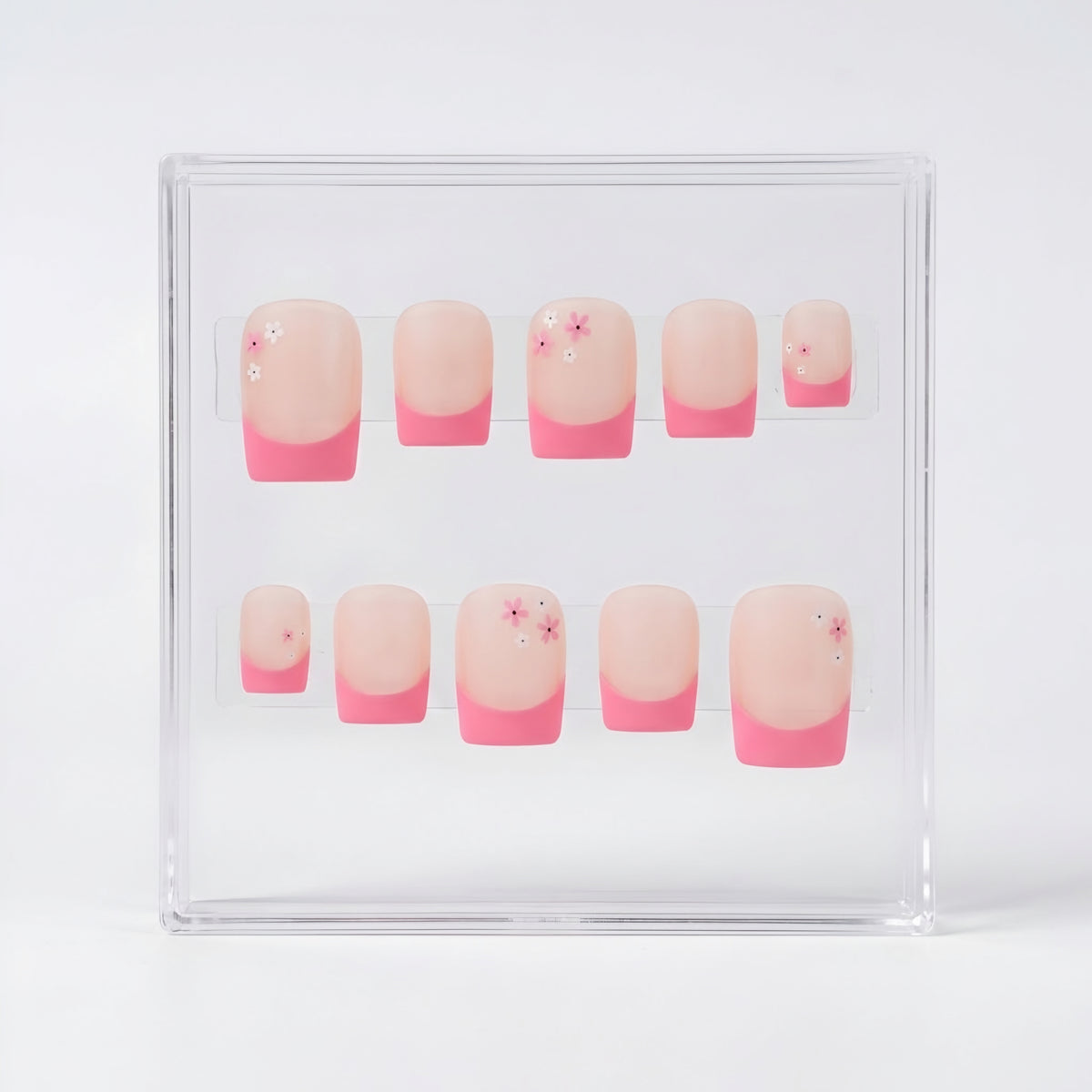 A set of ten square matte press-on nails displayed inside a clear plastic case on a white background. The nails feature a classic French manicure with a nude/pink base and  pink tips, with three nails decorated with tiny pink and white flower details.