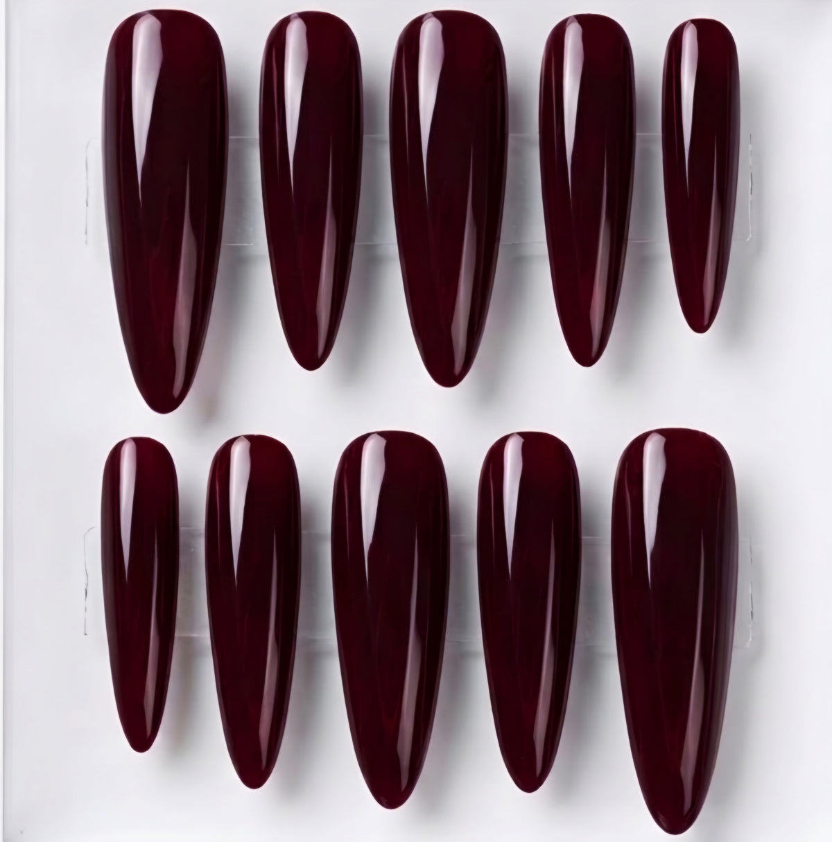 Ten glossy almond-shaped press-on nails in a deep burgundy shade, arranged in two rows on a clear plastic display card against a white background.