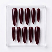 Ten glossy almond-shaped press-on nails in a deep burgundy shade, arranged in two rows inside a clear plastic display box on a white background.