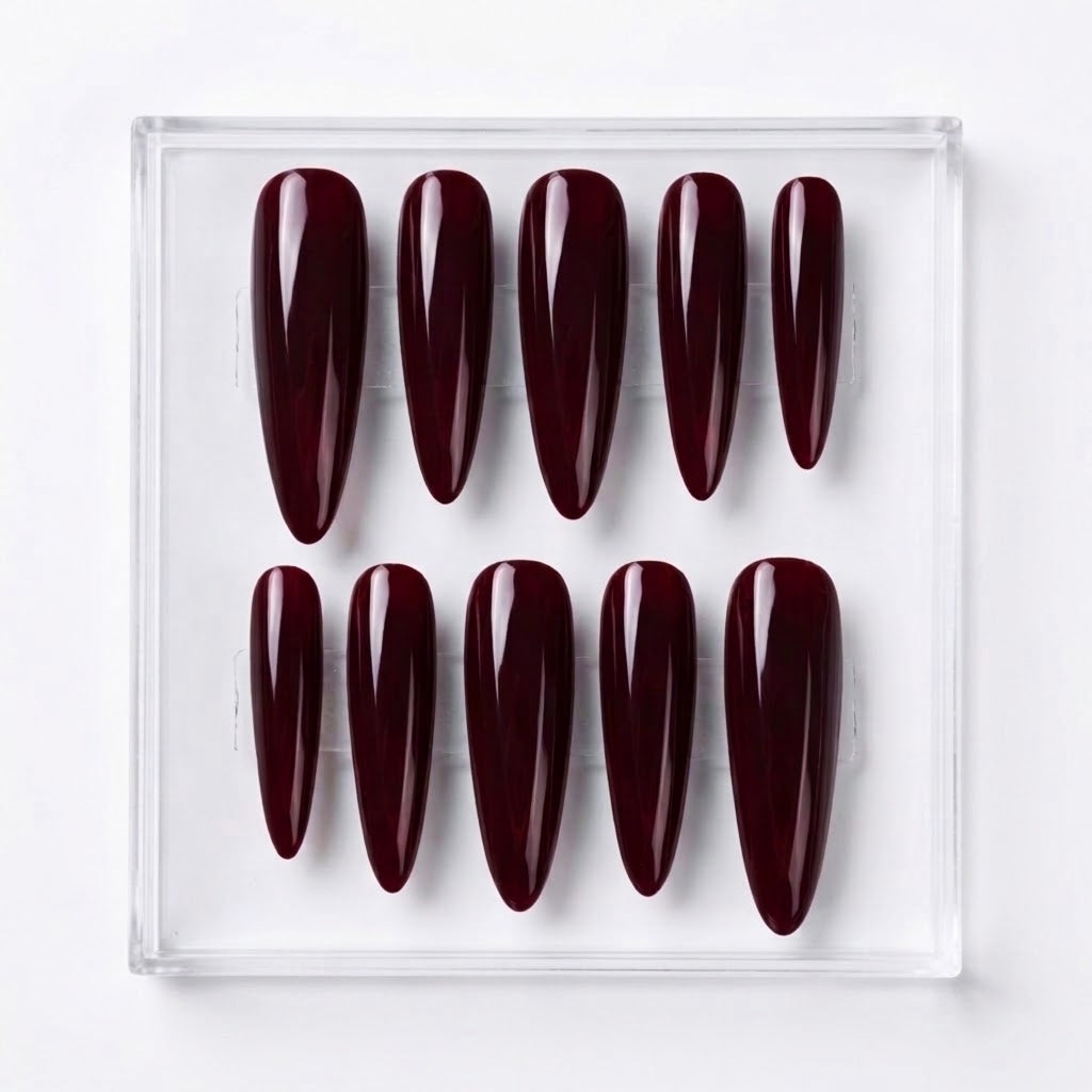 Ten glossy almond-shaped press-on nails in a deep burgundy shade, arranged in two rows inside a clear plastic display box on a white background.