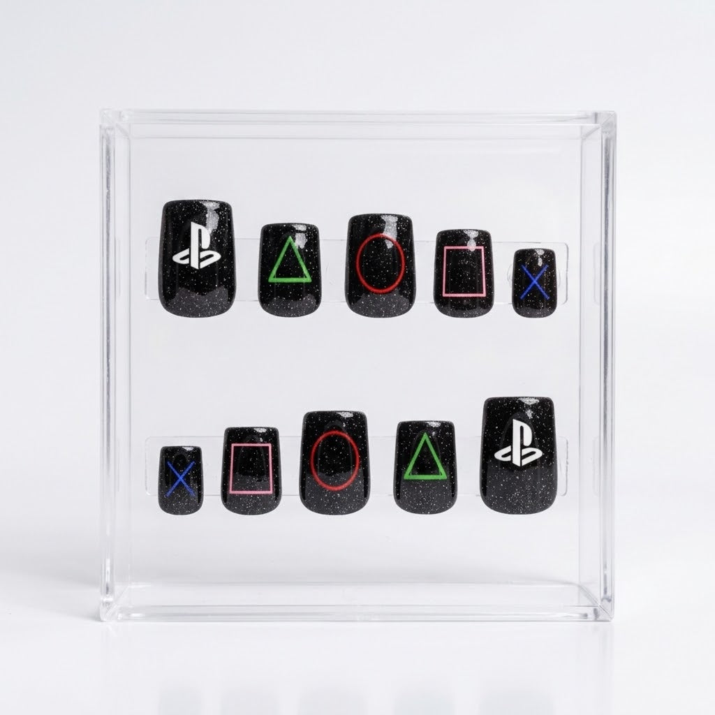 A set of 10 square black glitter press-on nails with PlayStation logo and symbol designs, displayed inside a clear acrylic box on a white background.