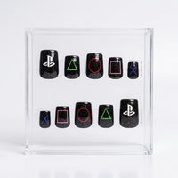 A set of 10 square black glitter press-on nails with PlayStation logo and symbol designs, displayed inside a clear acrylic box on a white background.