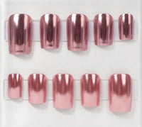 A set of metallic chrome rose gold press-on nails displayed on clear plastic stands against a white background.