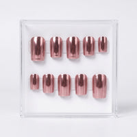 A set of metallic chrome rose gold press-on nails displayed in a clear acrylic case against a white background.