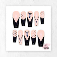 Glossy blush pink and black press-on nails with polka dots, bow nail art, and French tips in long coffin shape.