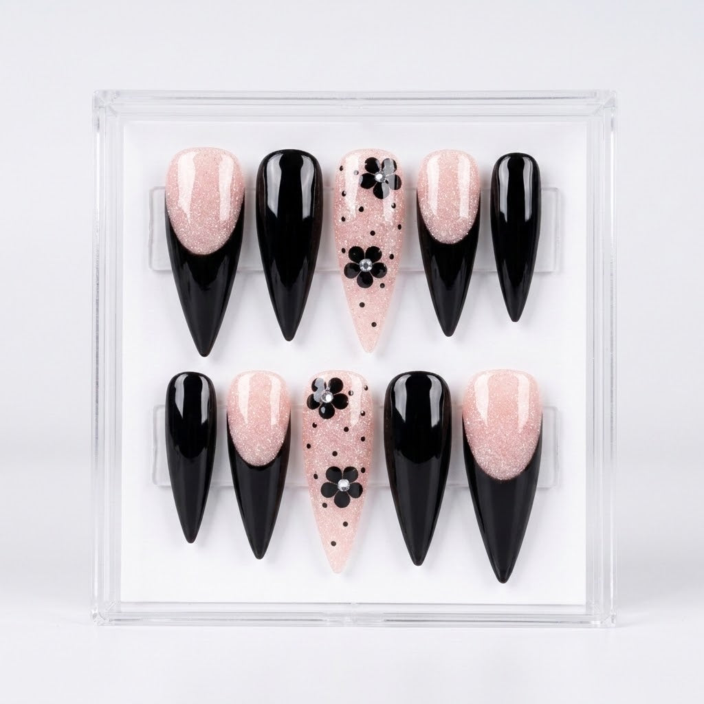 A set of 10 false press-on nails displayed in a clear plastic case against a white background. The nails feature a mix of glossy black stiletto shapes, glittery pale pink stiletto shapes, and pale pink almond-shaped nails decorated with black floral motifs and polka dots.