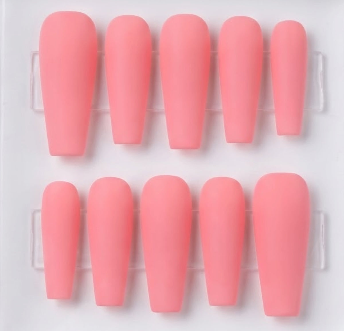Ten pink press-on nails arranged in two rows of five on a clear plastic display tray against a white background.