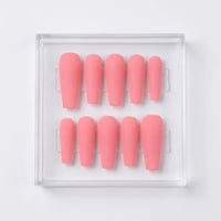 A set of ten matte pink press-on nails arranged in two rows inside a clear plastic display box on a white background.