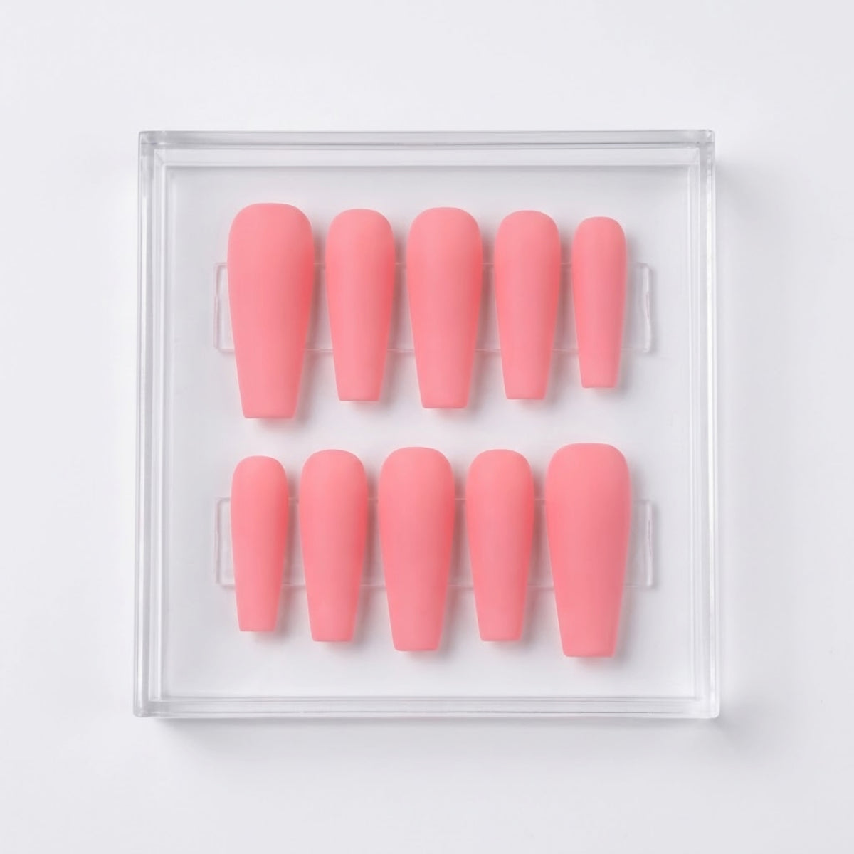 A set of ten matte pink press-on nails arranged in two rows inside a clear plastic display box on a white background.