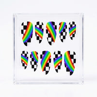 A clear acrylic nail display block containing ten almond press-on nails. Each nail features a black-and-white checkered pattern with a vibrant diagonal rainbow stripe running through the center.